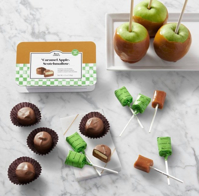 Caramel apples and candy on sticks with a packaging box on a marble surface