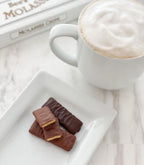 White mug with cappuccino and chocolate bars on a white plate