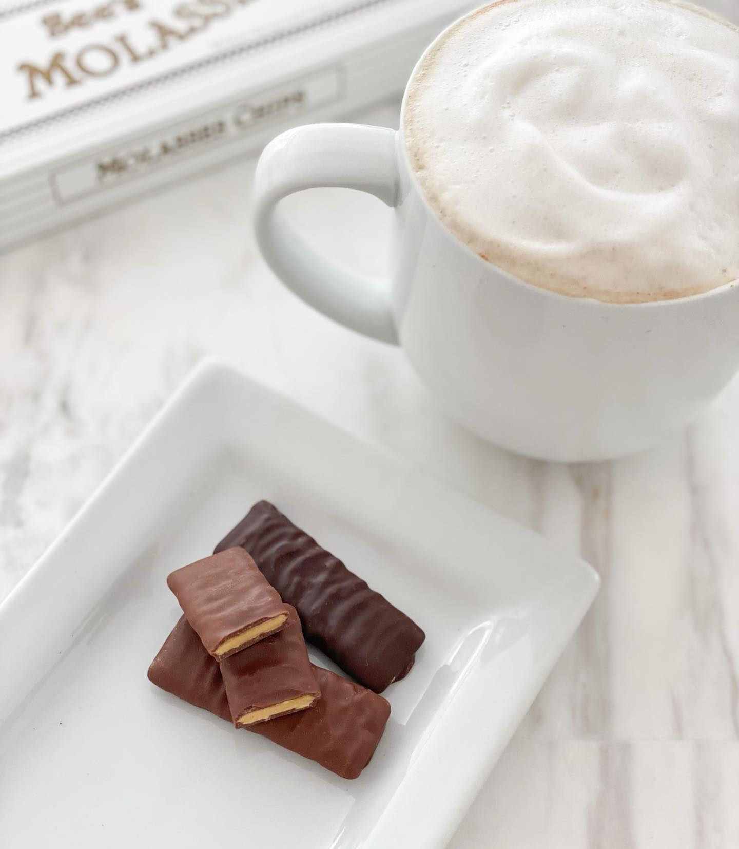 White mug with cappuccino and chocolate bars on a white plate