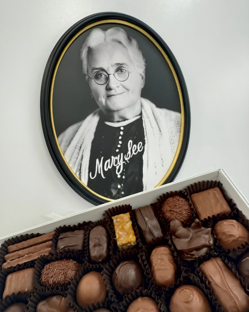 Box of chocolates with a framed portrait of an Mary See woman in the background