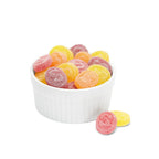 White bowl filled with colorful See's fruit medallions gummy candies on a white background