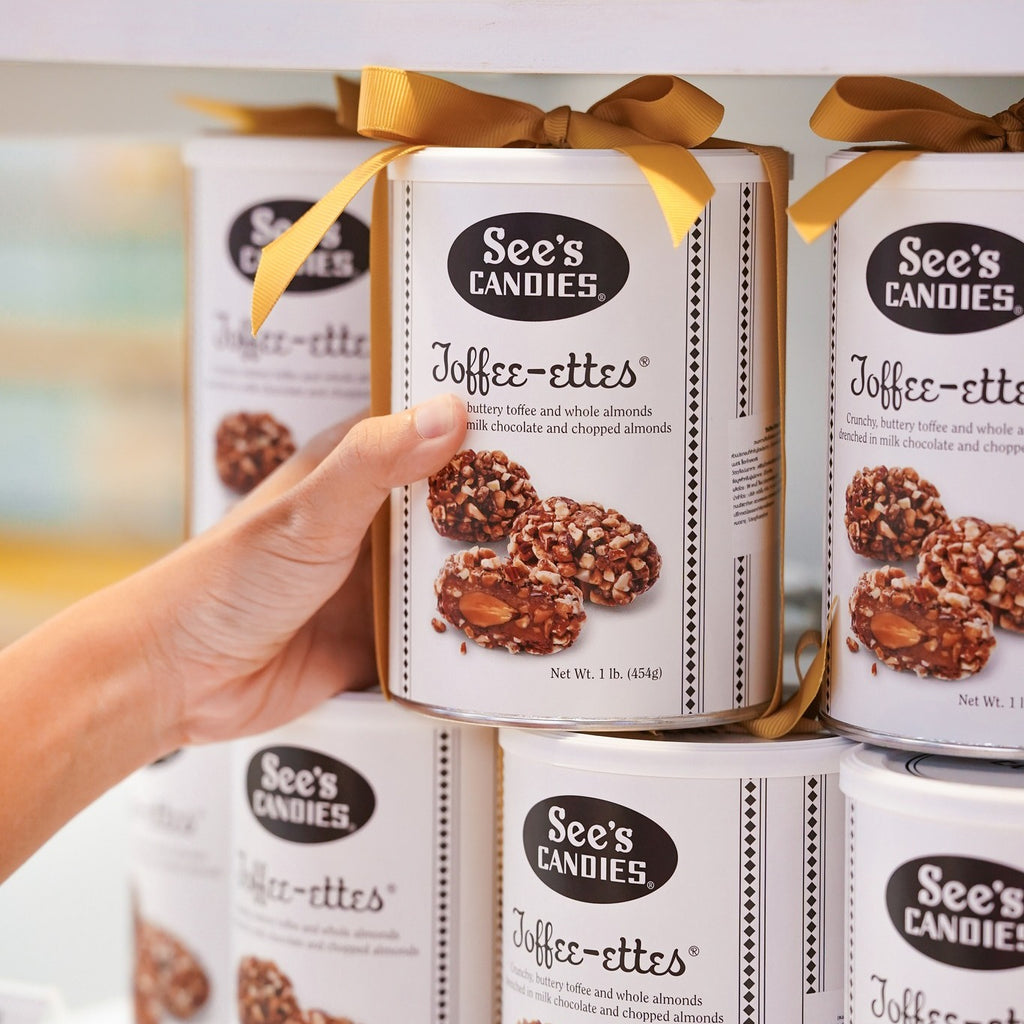 Hand holding a box of See's Candies Toffee-ettes with other boxes in the background.