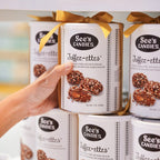 Hand holding a box of See's Candies Toffee-ettes with other boxes in the background.
