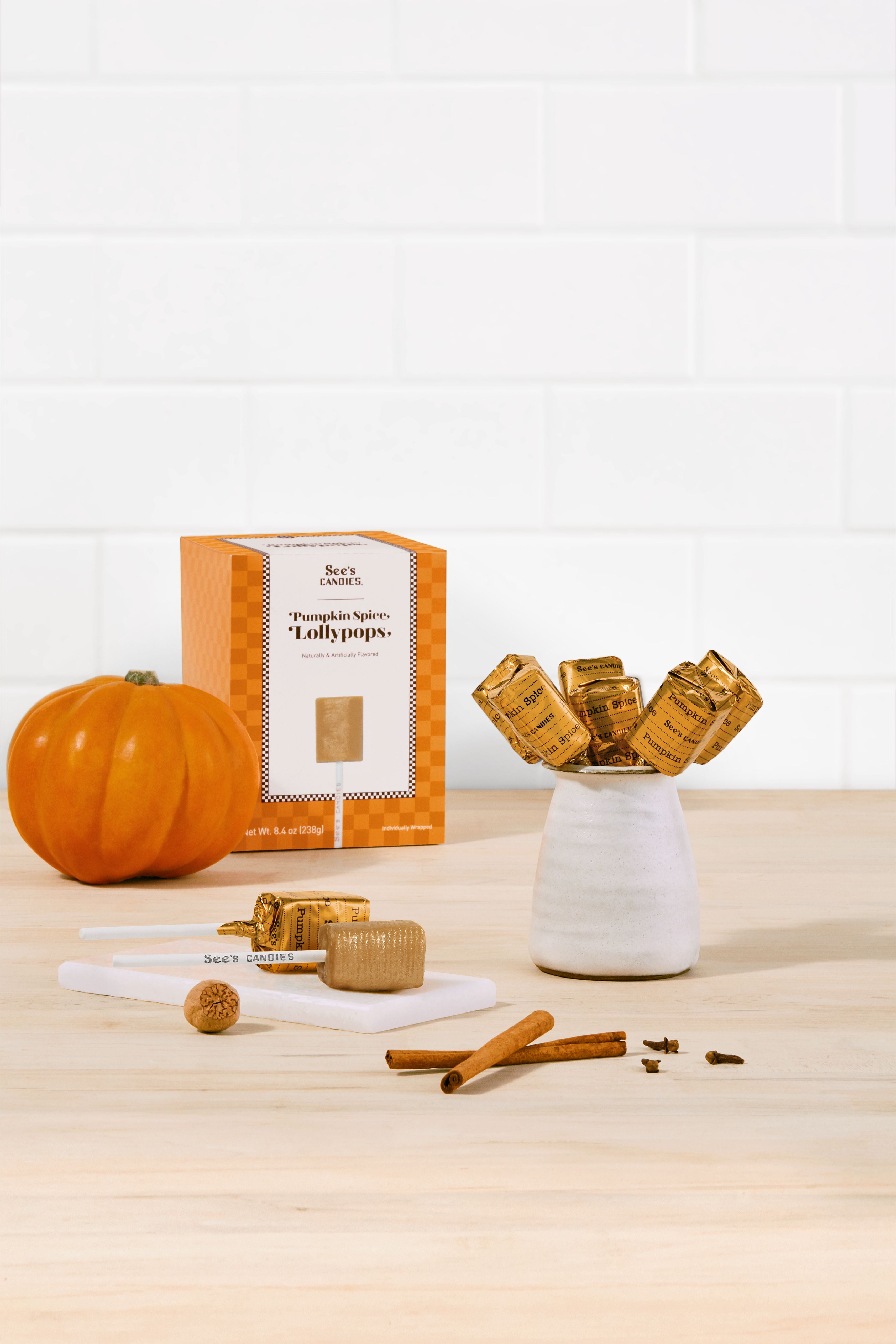 Pumpkin spice lollipops with packaging and cinnamon sticks on a wooden surface.