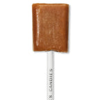 Caramel colored lollypop candy on a stick with 'See's Candies' branding on a white background