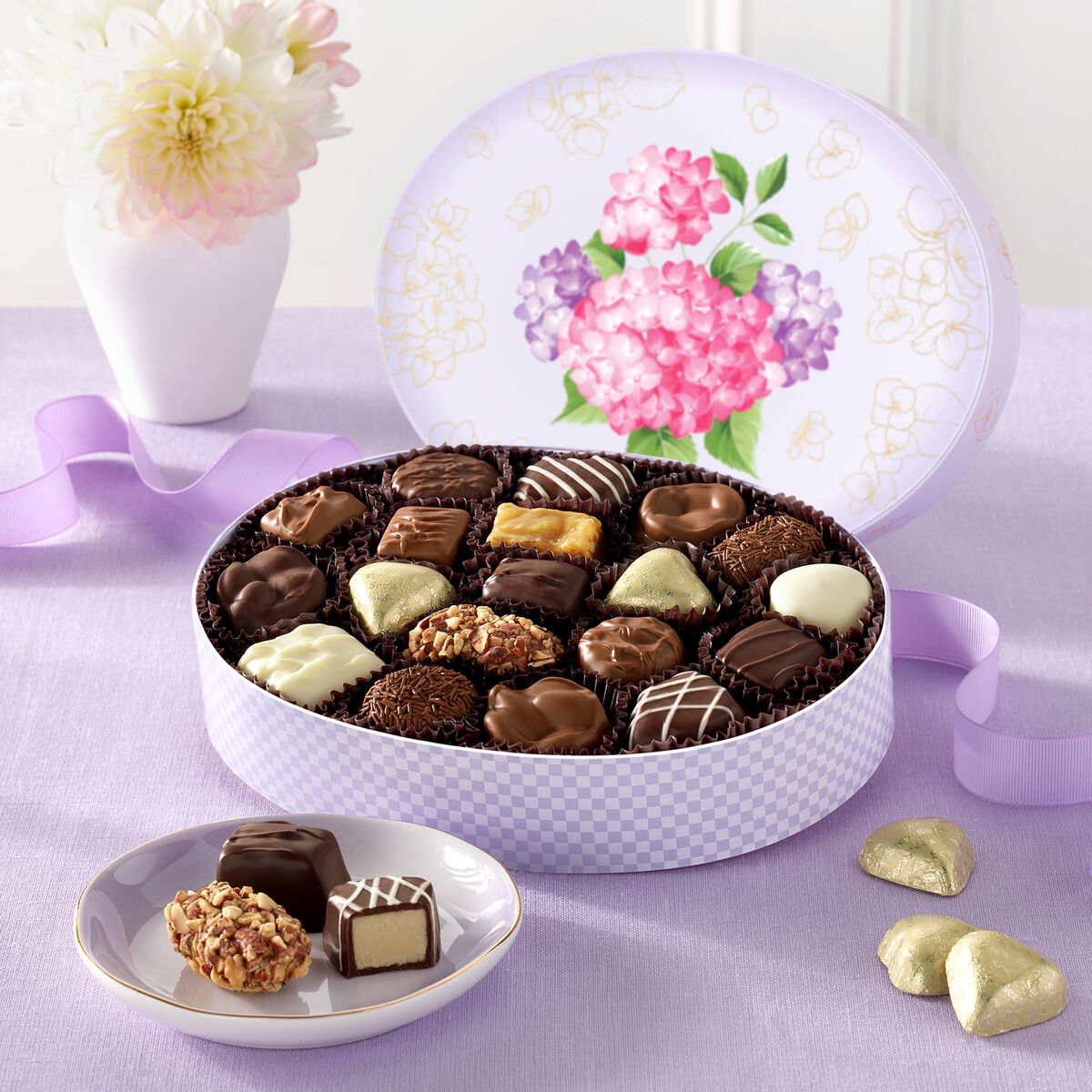 Assorted mother's day wisteria chocolates in a decorative box with a floral design on a purple tablecloth.